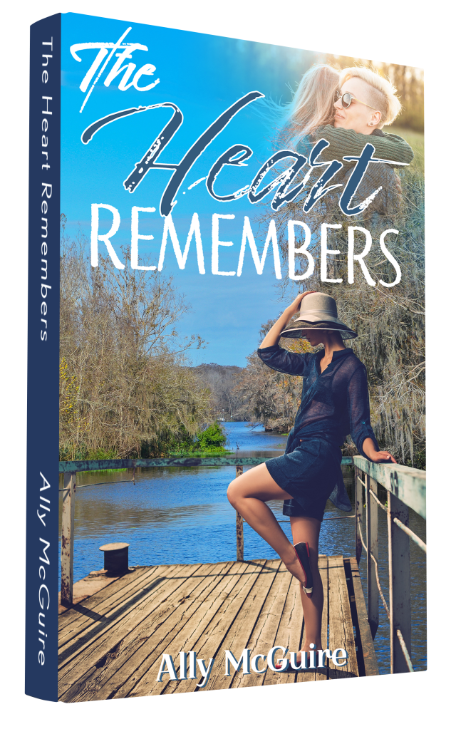 The book cover for The Heart Remembers has a side profile of a woman wearing a short navy blue dress and a straw hat. she's got one hand on the hat. There's a bayou in the background with spanish moss trees.